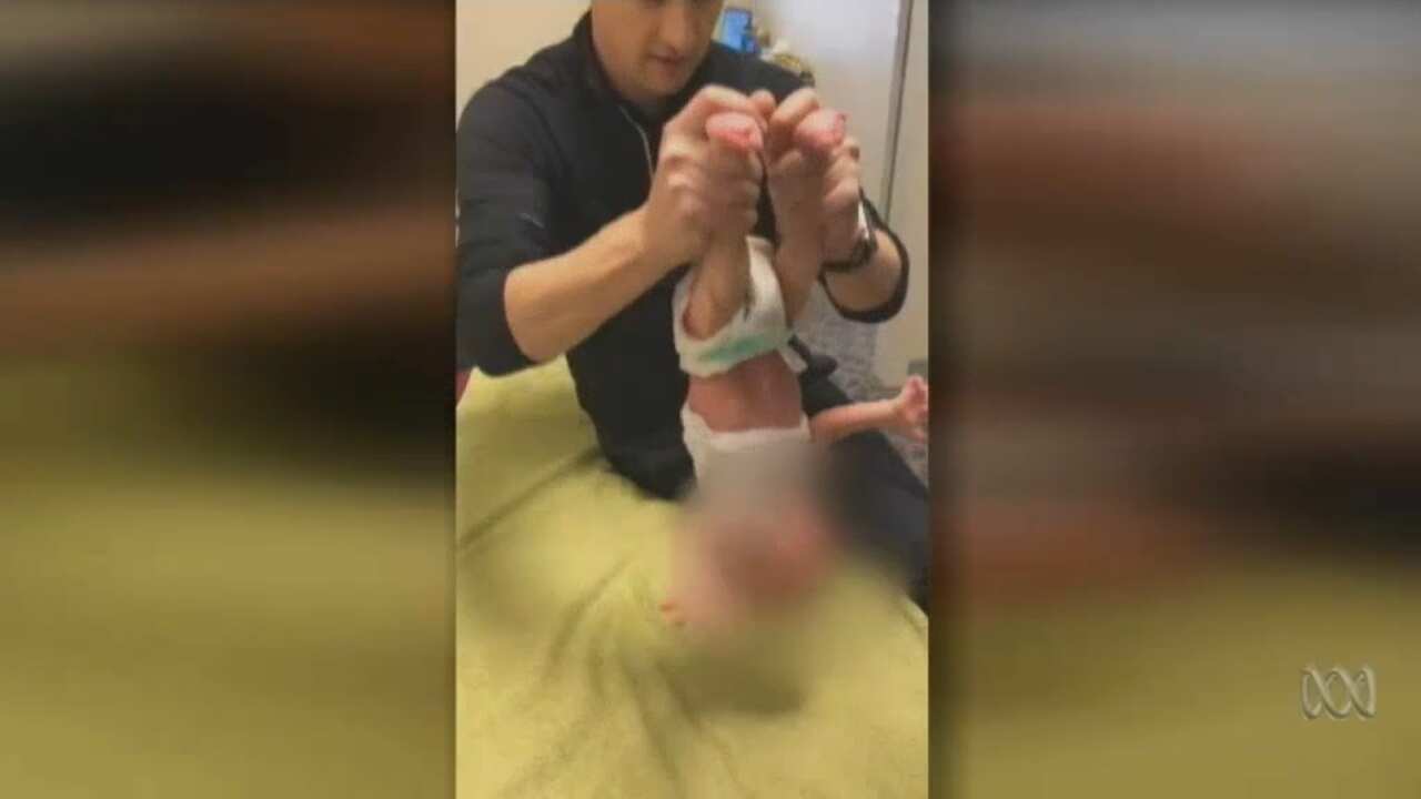 The video shows the chiropractor holding the baby by it's feet. 