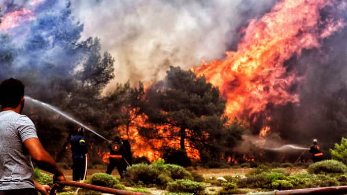 Firefighters and volunteers try to extinguish a wildfire raging in Verori.