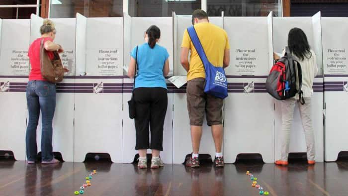 Rear view of four people standing at voting booths in Australia