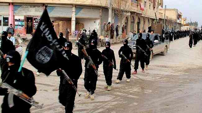 Armed Islamic State militants marching in black through an intersection. 
