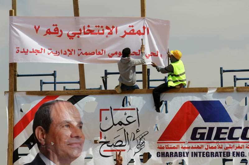 A worker hangs a banner reading 'This place is for voting' above a photo of Egyptian President Abdel Fattah al-Sisi during day one of the vote.