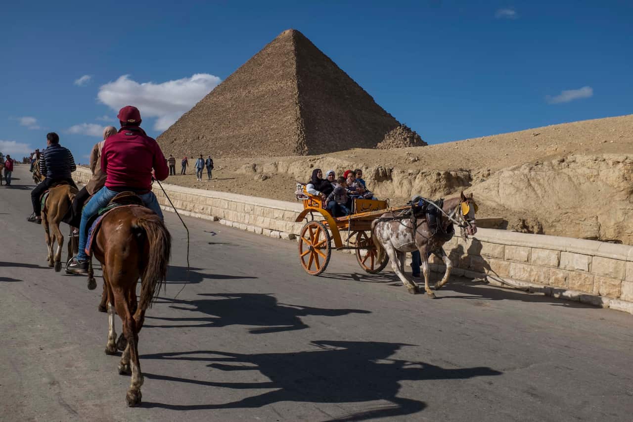 Tourists ride on horses and carriages near the Egyptian pyramids.