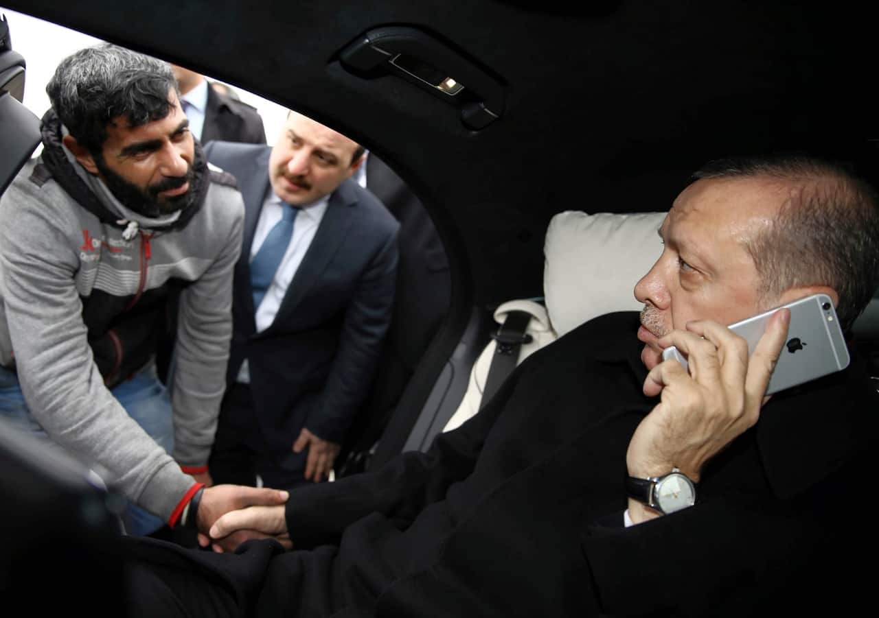 Dec. 25, 2015 file photo, Turkey's President Recep Tayyip Erdogan, right, holds Turkish citizen Vezir Cakras by the hand while speaking on his mobile phone