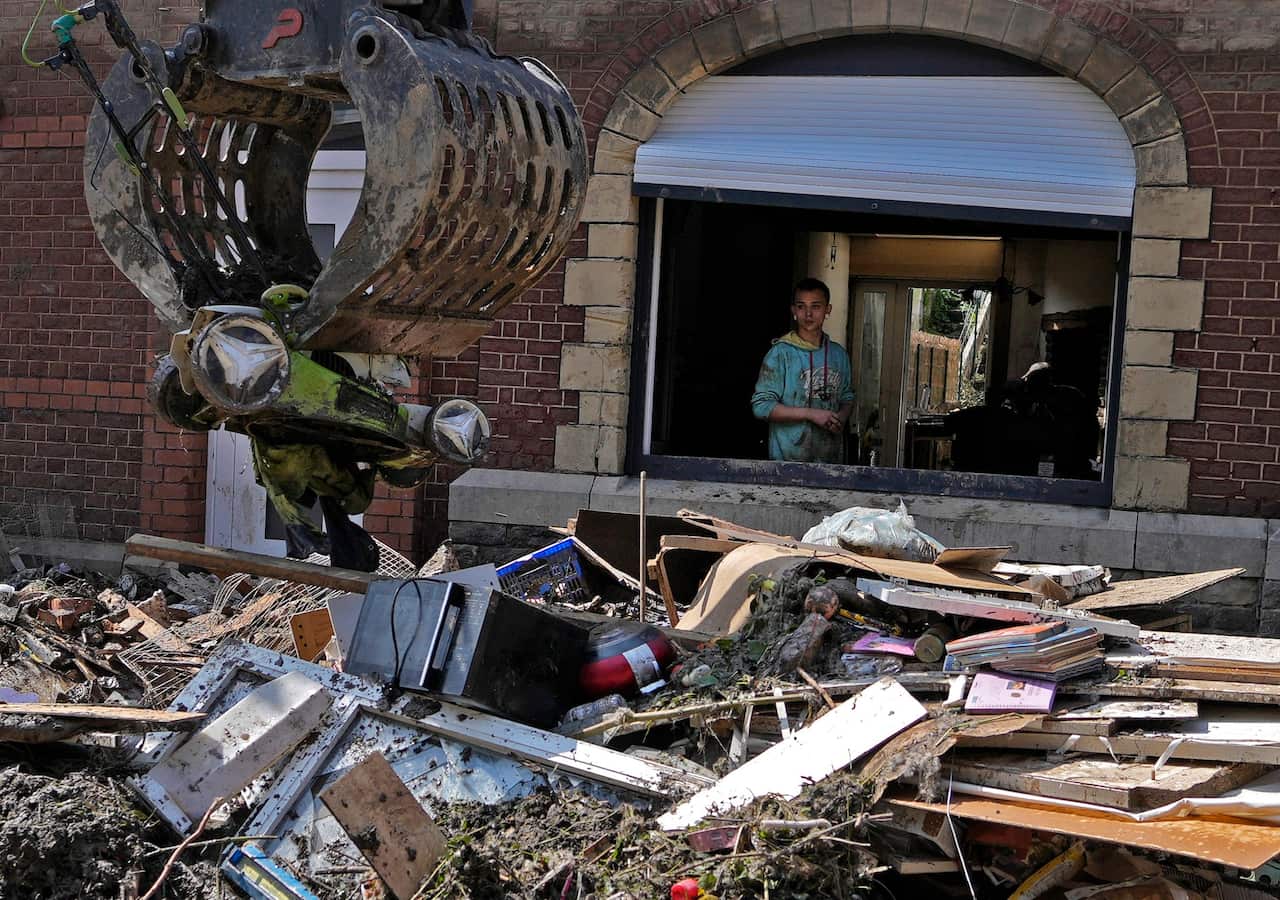 A resident watches from his window as a crane takes away damaged belonging after flooding in Drolenvol, Belgium.