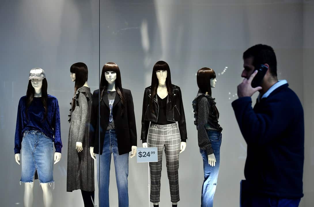A man walks past a shop window containing several mannequins dressed in cheap fashionable clothes.