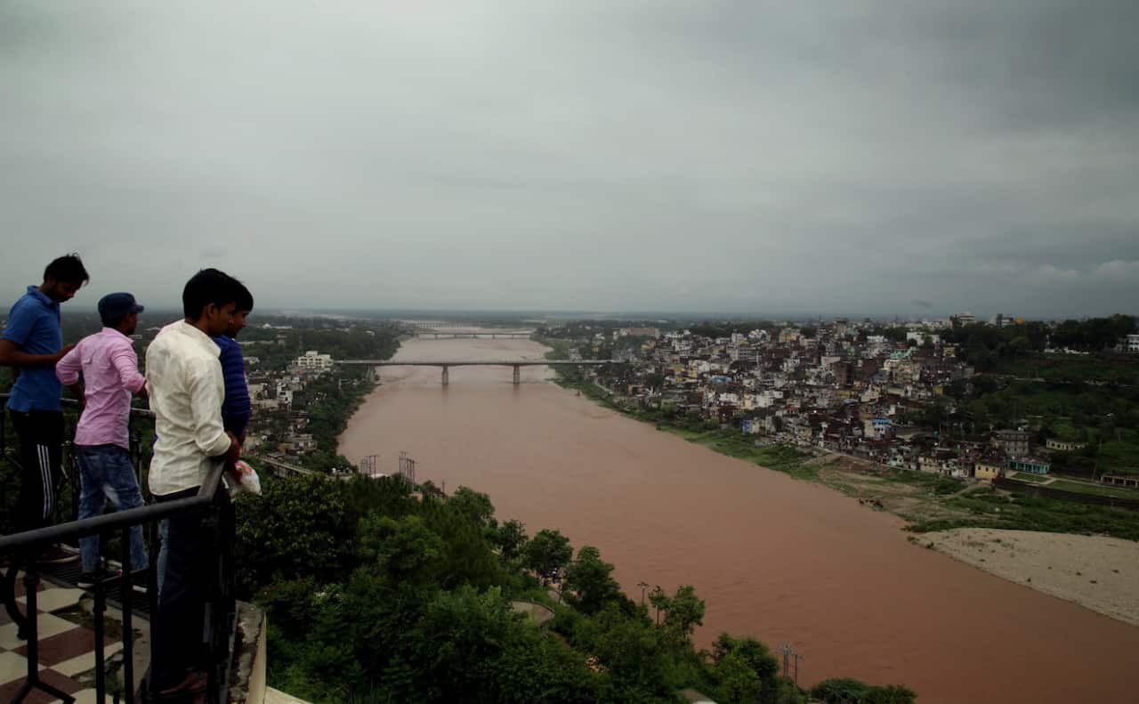 Indian people look at a flooded river as monsoon clouds cover the sky over the old city situated on the banks of the Tawi river in Jammu