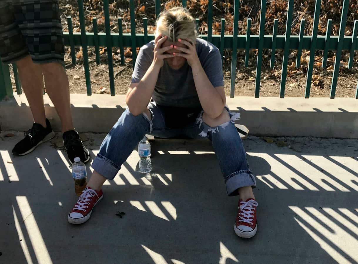 An unidentified woman sits next to witnesses on a sidewalk after a gunman barricaded himself inside a Trader Joe's store in Los Angeles