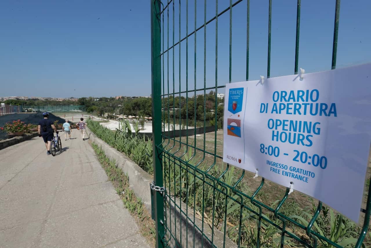 People walk through the gate of the newly opened "Tiberis" beach along the Tiber river in Rome, Sunday, Aug. 5, 2018.