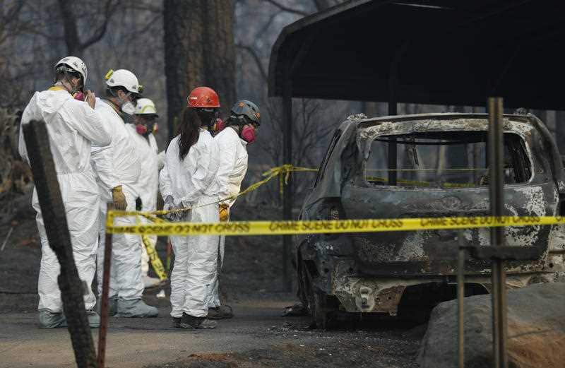 Search and rescue personnel peer into a car with suspected human remains at the Camp Fire grounds.