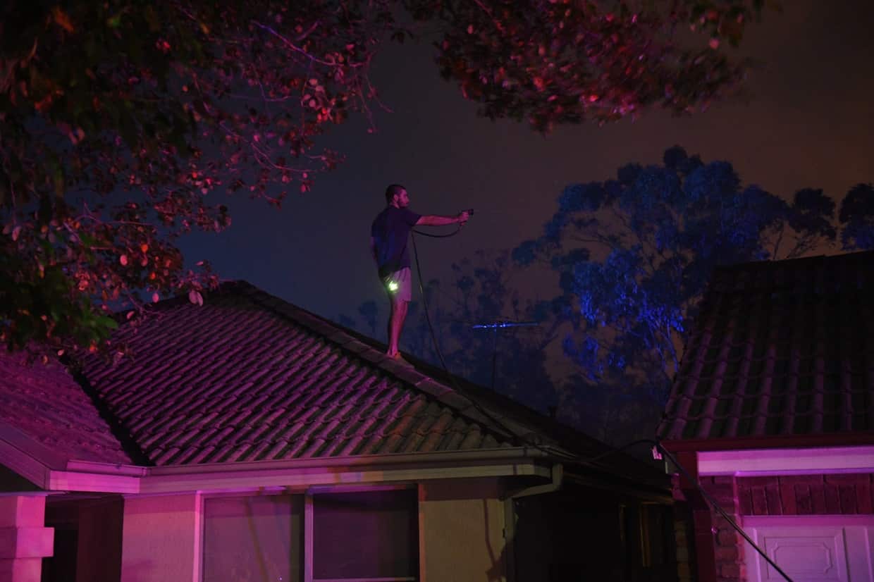 Local resident Jordan Dodin climbs onto a roof to protect the house from fire in Wattle Grove on Saturday night.