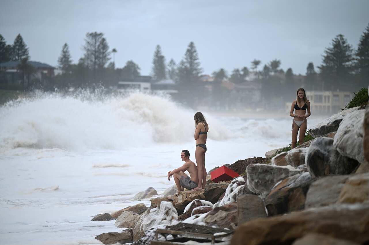 Swimmer watch from the rocks as sea foam brought by waves approaches Collaroy.