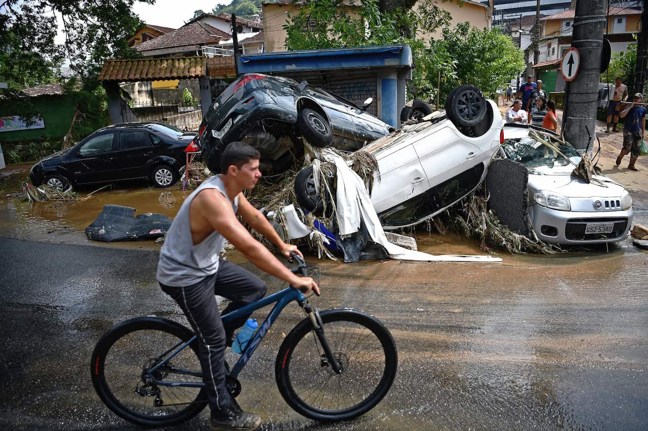 A man rides his bicycle past cars destroyed by a flash flood in Petropolis, Brazil.