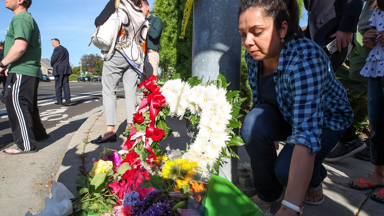 A woman leaves flowers at small memorial near Chabad of Poway, where a man with a gun shot multiple people inside the synagogue.