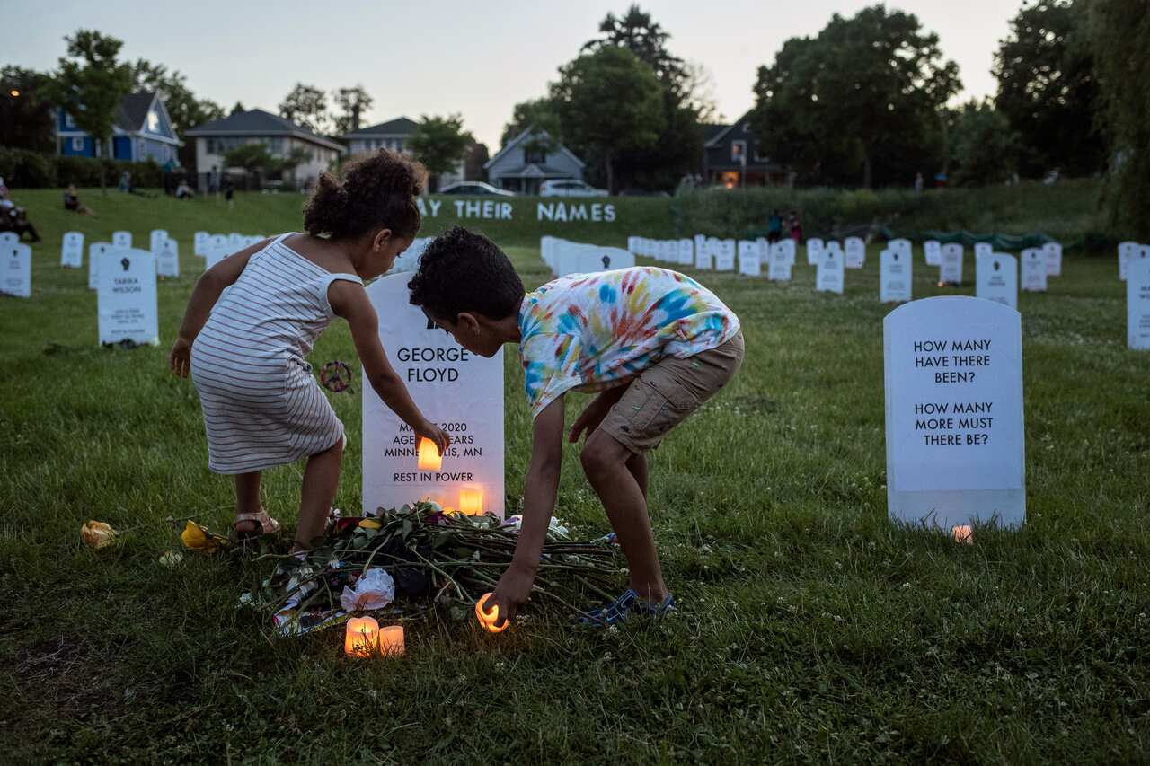 Children put lights in front of a mock headstone bearing the name of George Floyd at a makeshift memorial to people killed by the police in Minneapolis