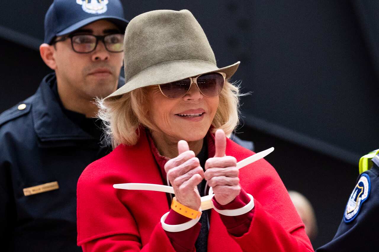 Fonda flashes the thumbs up as she's escorted away by police. 