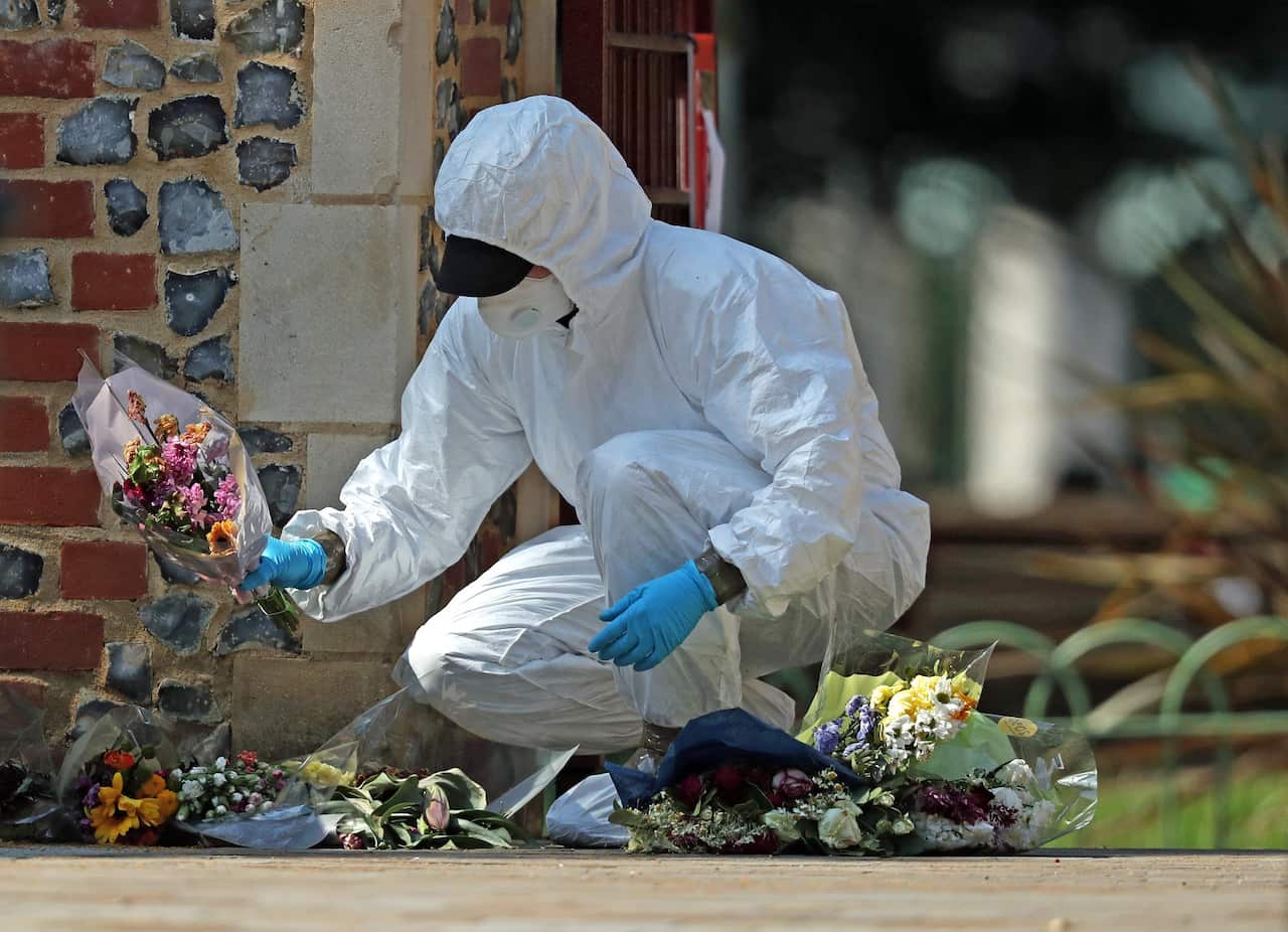 A forensic officer searches floral tributes laid at Forbury Gardens, in Reading town centre.
