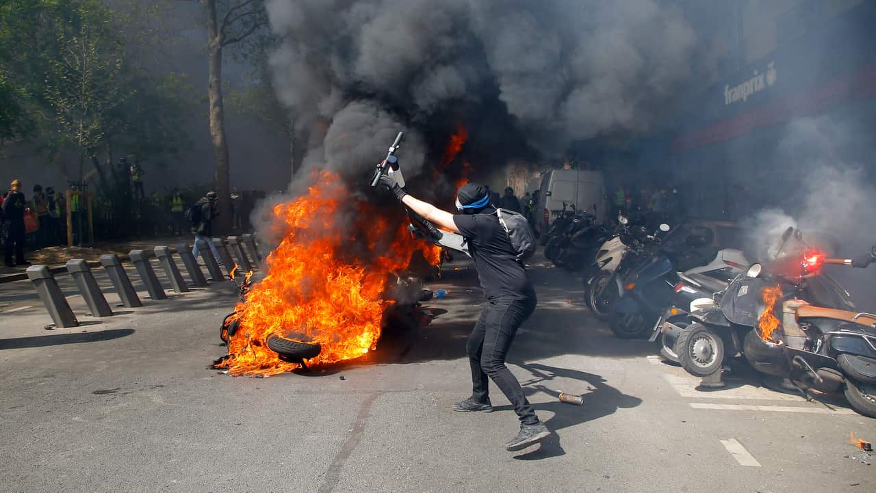 A protester throws a scooter onto a pile of burning motorbikes during a yellow vest demonstration in Paris.