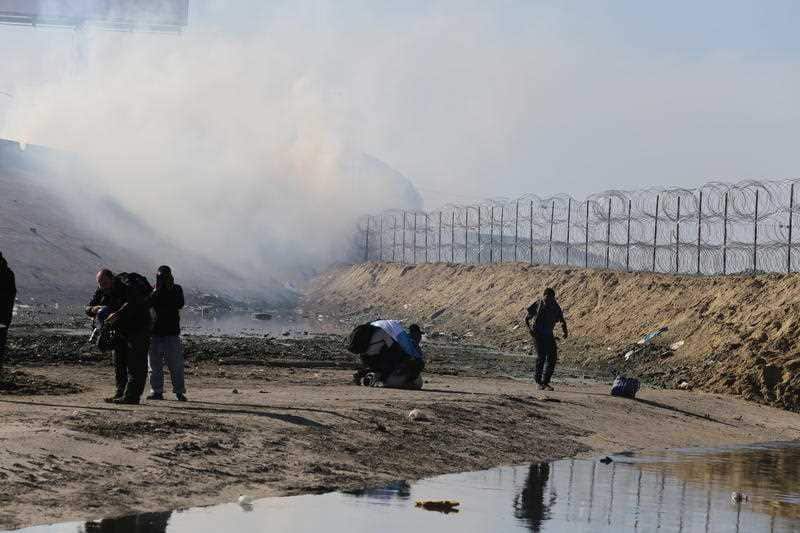 Migrants run from the cloud of tear gas.