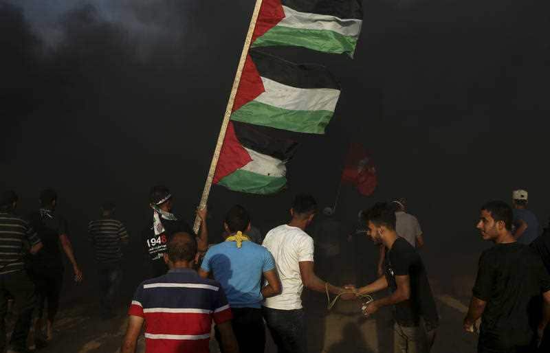 A protester waves Palestinian national flags while others burn tires near the fence of the Gaza Strip border with Israel.