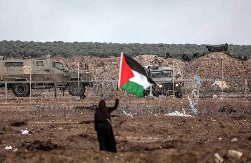 A Palestinian protester waves a Palestinian flag in front of Israeli soldiers during the clashes on Friday.