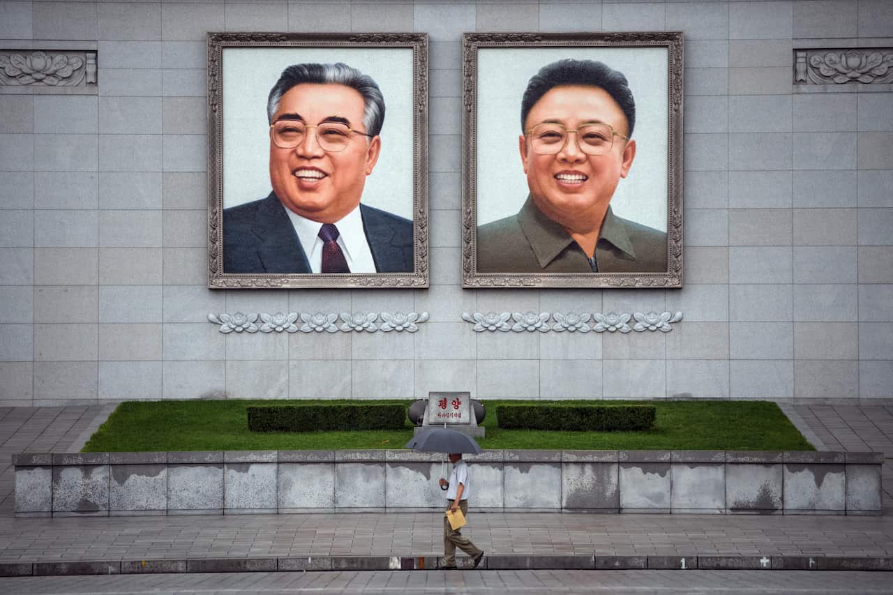 People walk beneath large images of Kim Il-sung and Kim Jong-il displayed in Kim Il-sung Square.