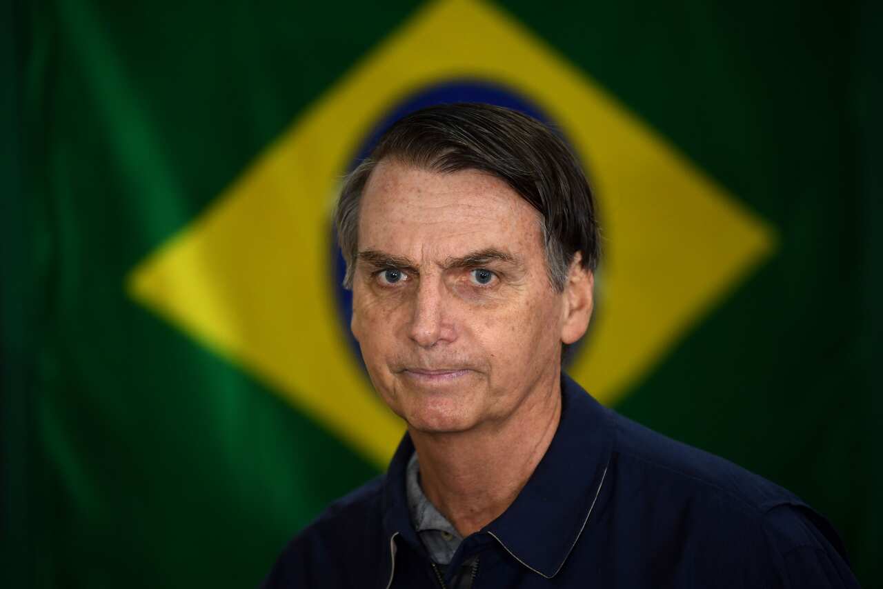 Brazil's right-wing presidential candidate for the Social Liberal Party (PSL) Jair Bolsonaro walks in front of the Brazilian flag as he prepares to cast his vote during the general elections, in Rio de Janeiro, Brazil, on October 7, 2018. - Polling statio