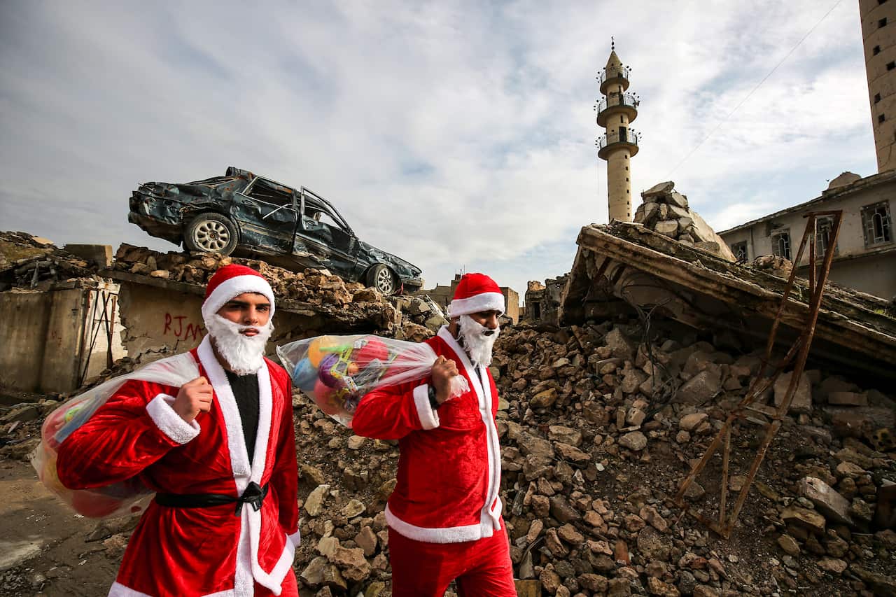 Iraqi youths dressed in Father Christmas suits walk through the streets of the old city of Mosul as they distribute gifts.