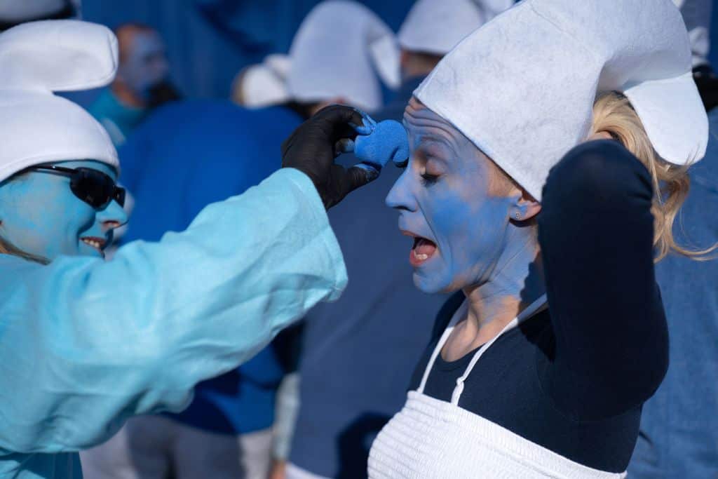 A participant has her face painted in blue before a gathering of people dressed as Smurfs.