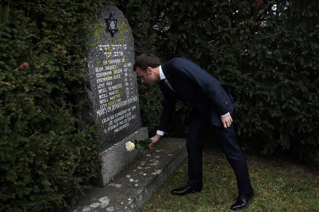 French President Emmanuel Macron lays a white rose on a grave vandalised with swastikas.