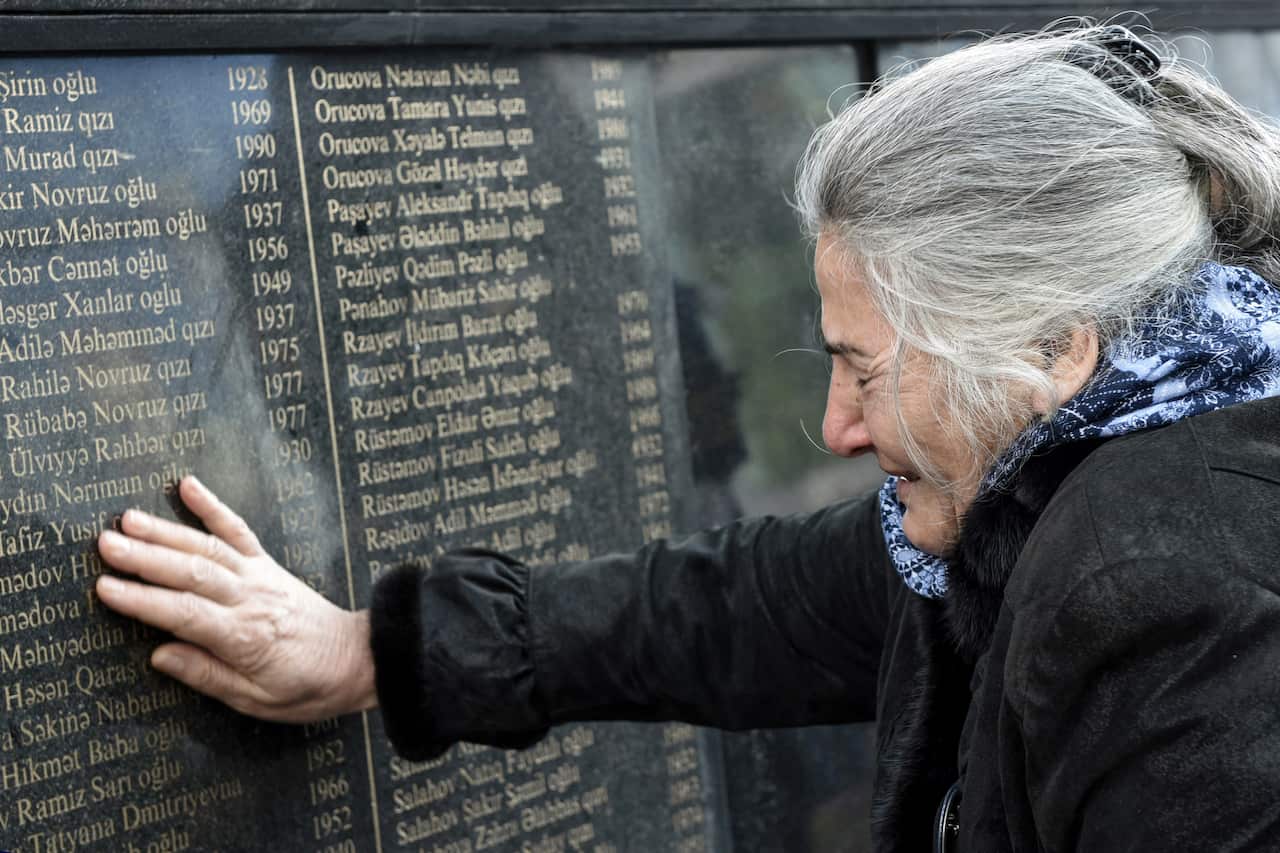 A woman cries as she touches a plaque with names of the deceased.