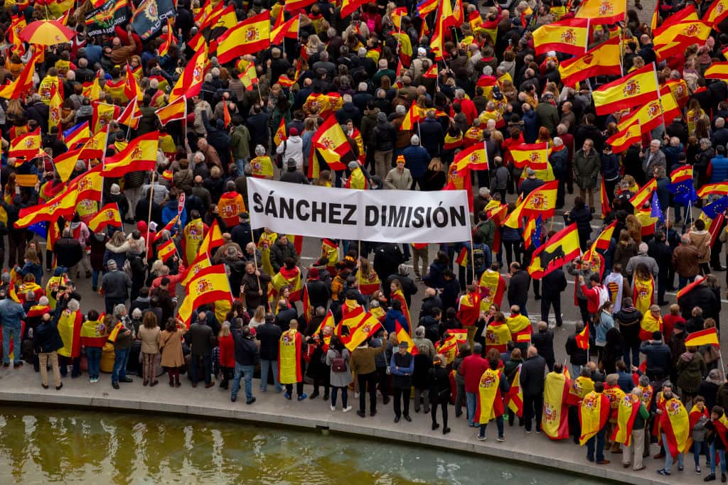 Protesters hold a banner reading "Sanchez resignation".