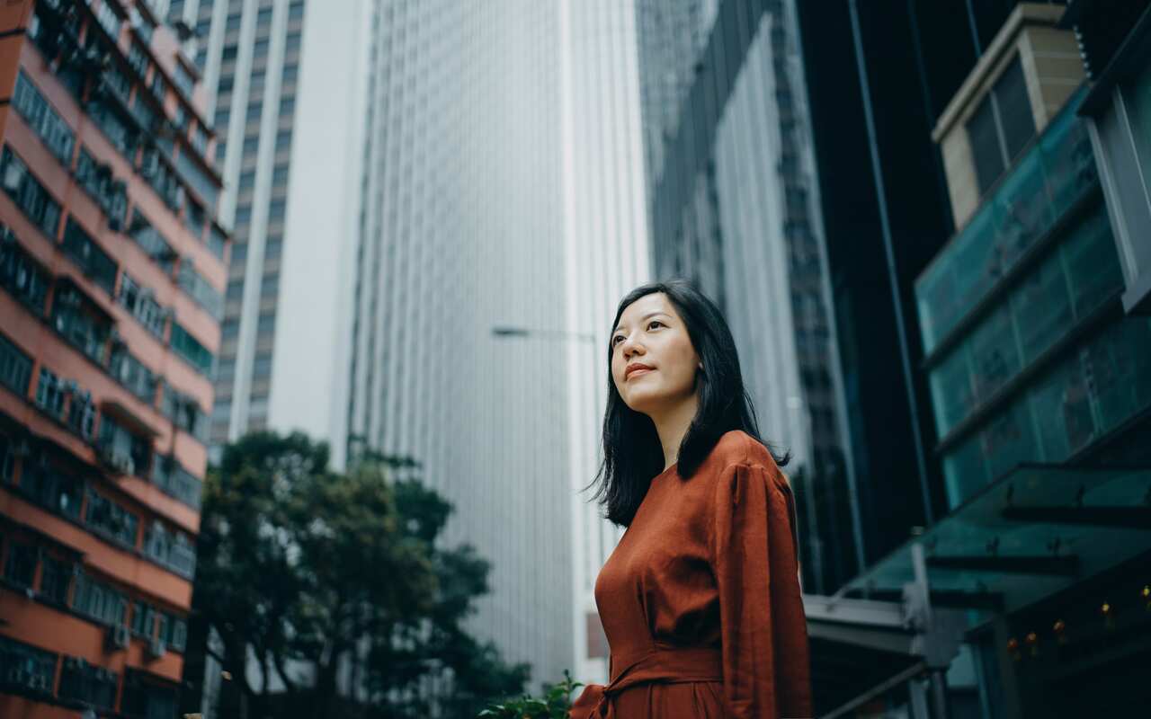 Low angle portrait of confidence young woman standing against highrise city buildings in city