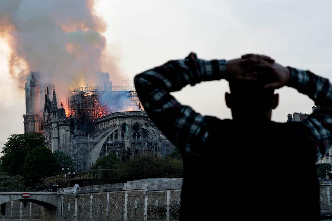 A man watches the landmark Notre-Dame Cathedral burn, engulfed in flames, in central Paris.