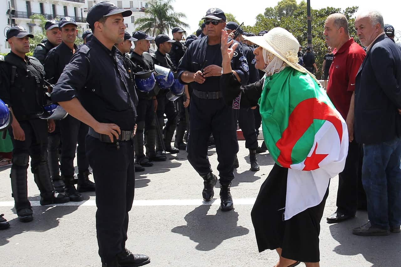 An Algerian protester wrapped with a national flag confronts riot police last month.