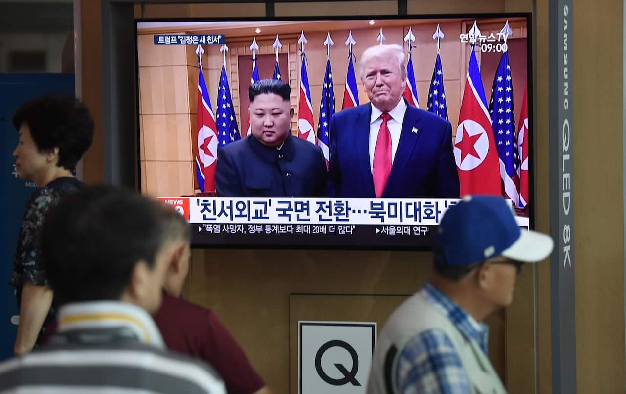 People watch a television news screen showing file footage of a meeting between US President Donald Trump and North Korean leader Kim Jong Un.