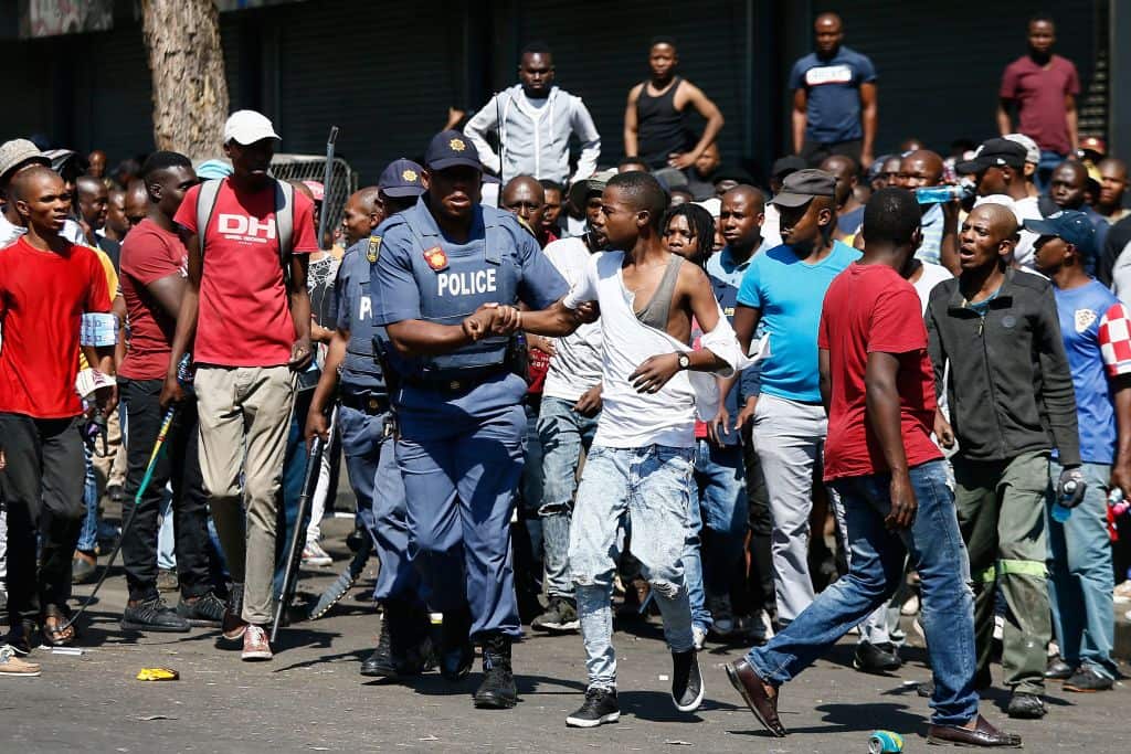 South African Police Service members rescue a man from angry taxi drivers during a riot near the Bloed Taxi Rank on August 28, 2019, in Pretoria
