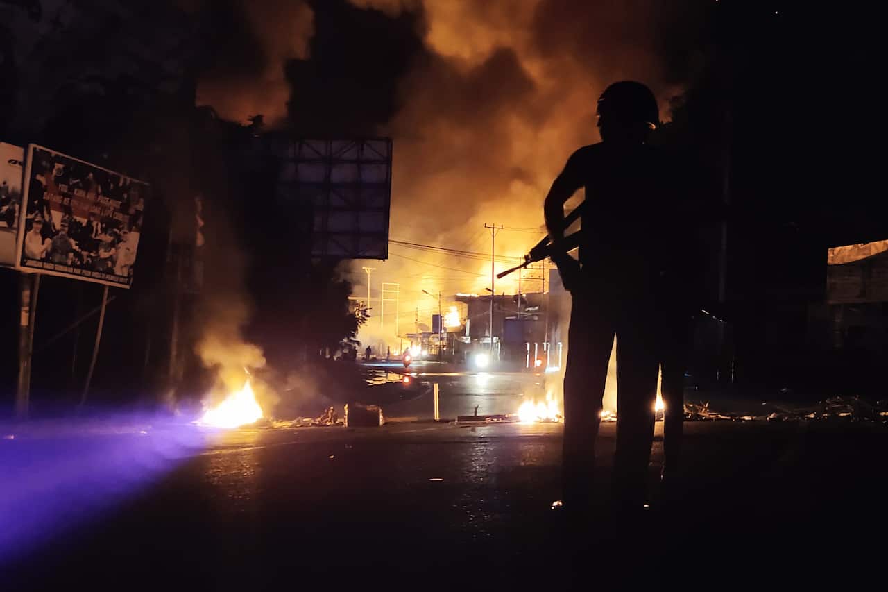 An armed Indonesian policeman stands guard near a burning building after hundreds of demonstrators marched near Papua's biggest city Jayapura.