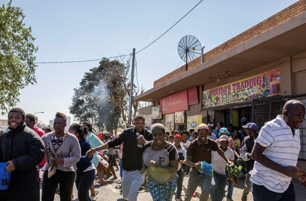 South African looters run off an alleged foreign-owned shop as South African Police officers intervene during a riot in the Johannesburg suburb of Turffontein on September 2, 2019 