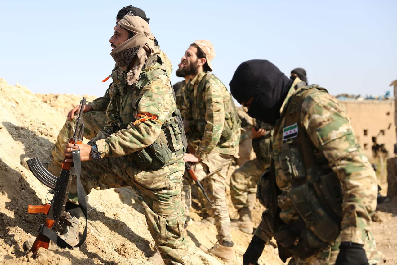 Turkish-backed Syrian rebels and Turkish soldiers watch as smoke billows from the border town of Ras al-Ain.