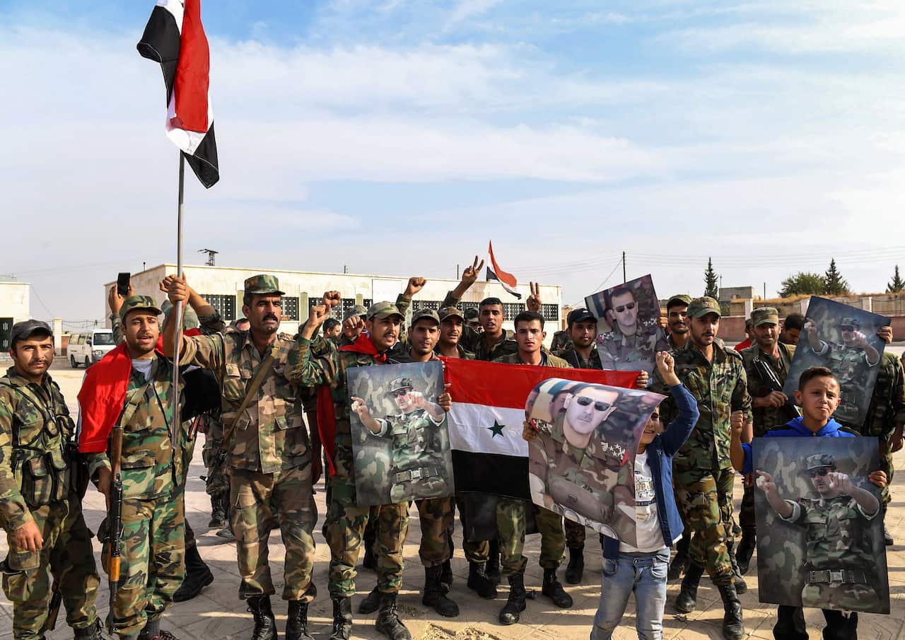 Syrian government soldiers pose for a group photo with national flags and portraits of President Bashar al-Assad on the outskirts of the northern city of Manbij