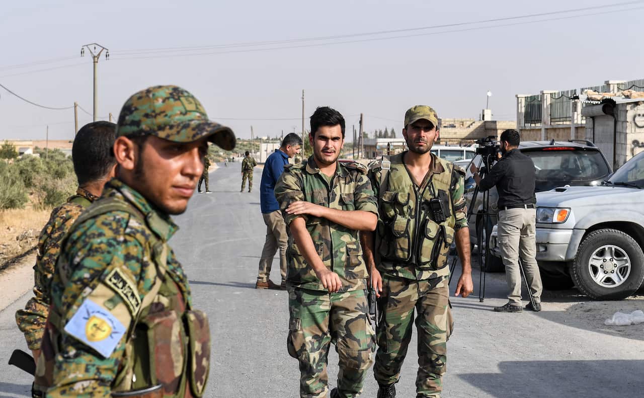 A fighter (L) bearing the insignia of the Manbij Military Council stands by as Syrian government soldiers walk past.
