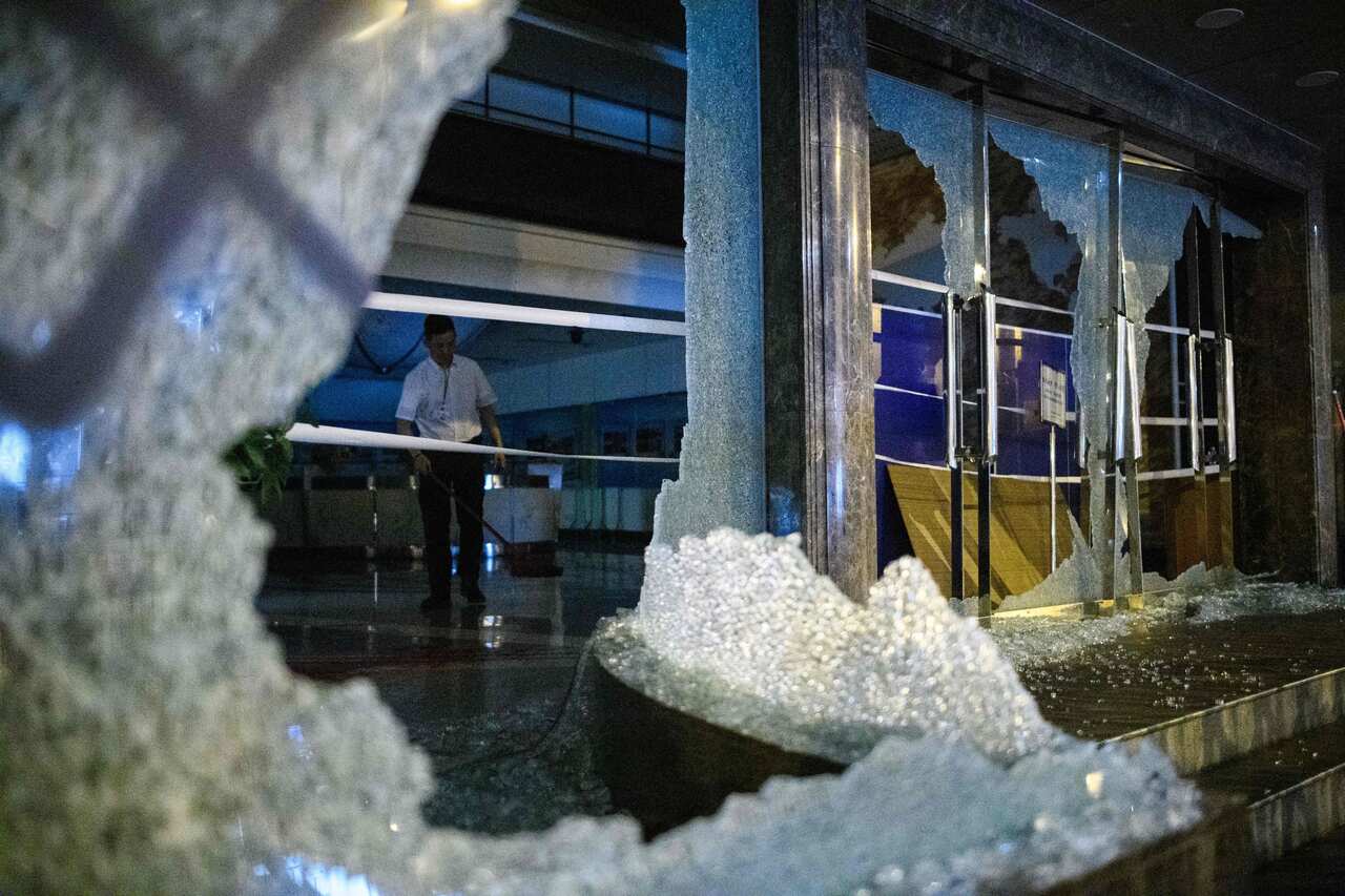 A security guard helps sweep up shattered glass inside China's Xinhua News Agency after it was damaged by protesters in the latest wave of Hong Kong protests.