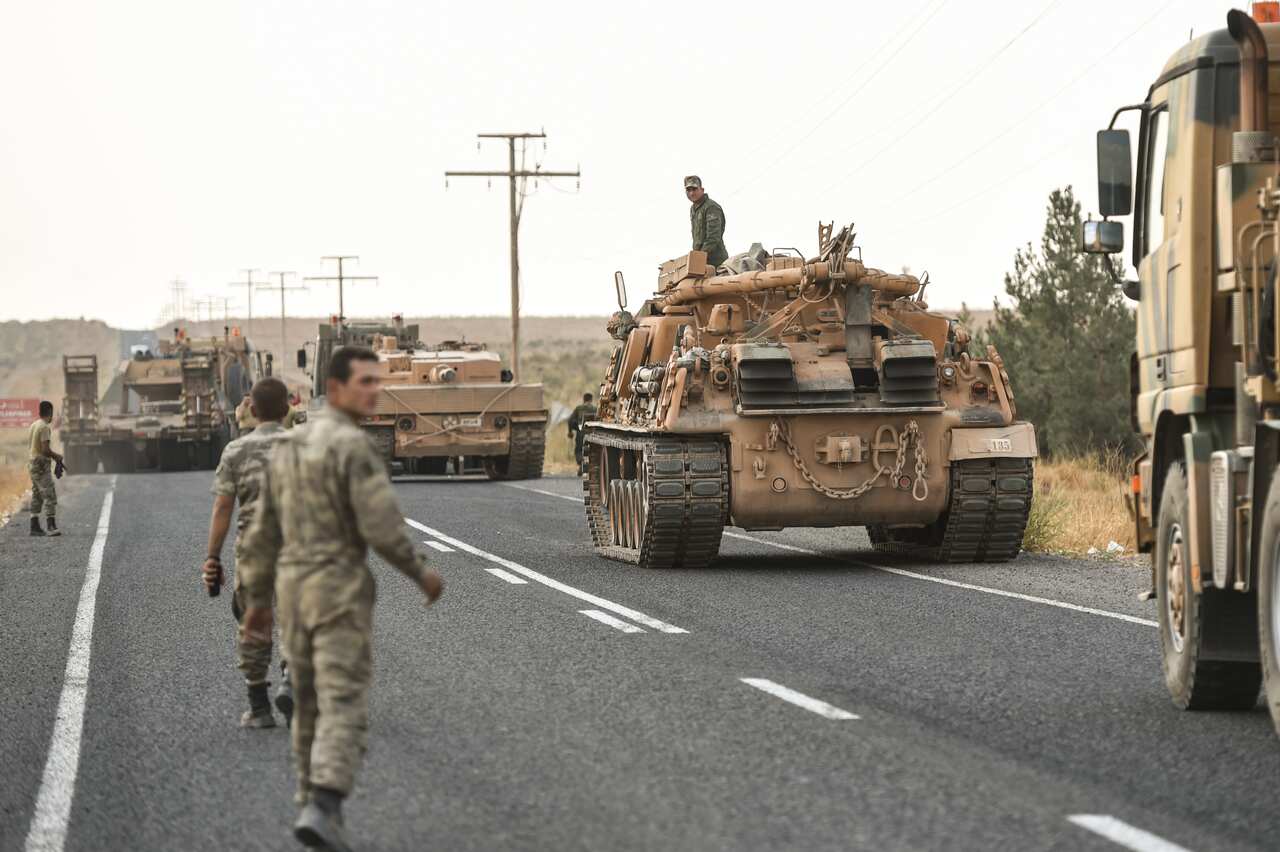 Turkish soldiers prepare their tanks and secure the road ahead of a move towards the Syrian border.