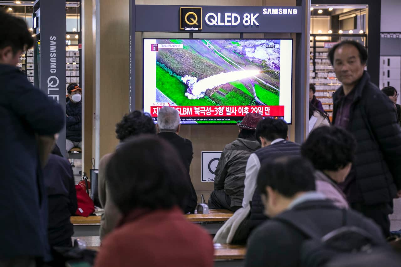 Travellers at Seoul Railway Station watch a television broadcast reporting a North Korean missile launch.