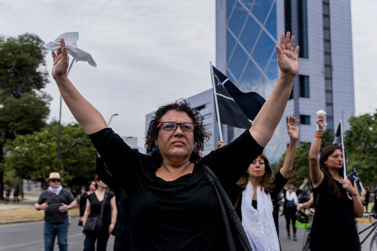 Women walk with their arms raised and dressed in black during a silent protest against the government of President of Chile Sebastián Piñera.