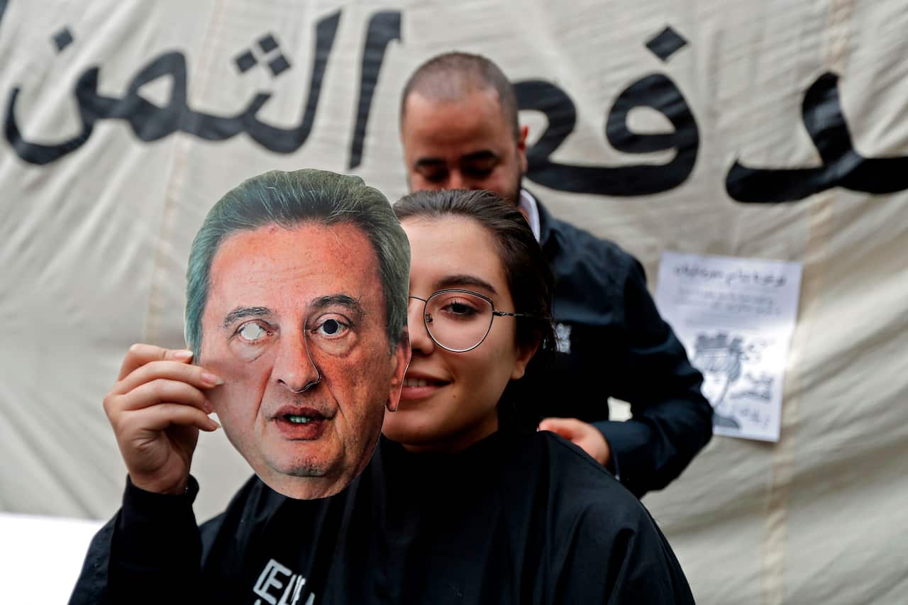 A Lebanese anti-government protester holds a mask of Lebanon's Central Bank Governor Riad Salameh as she sits for a haircut in front of the central bank HQ.