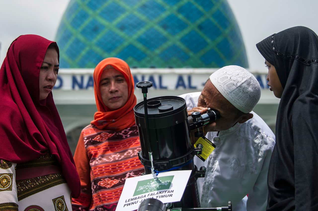 A Muslim family uses a telescope to watch the moon move in front of the sun in a rare "ring of fire" solar eclipse in Surabaya on December 26, 2019. (Photo by JUNI KRISWANTO / AFP) (Photo by JUNI KRISWANTO/AFP via Getty Images)
