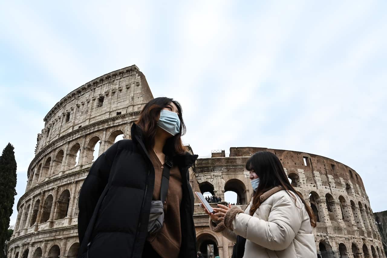 Tourists wearing protective respiratory masks tour downtown Rome.