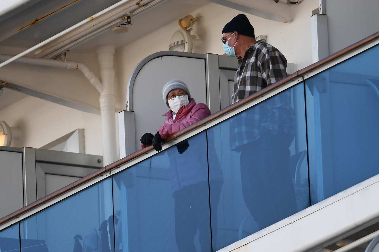 Quarantined passengers wearing protective face masks stand on a balcony of the Diamond Princess cruise ship.