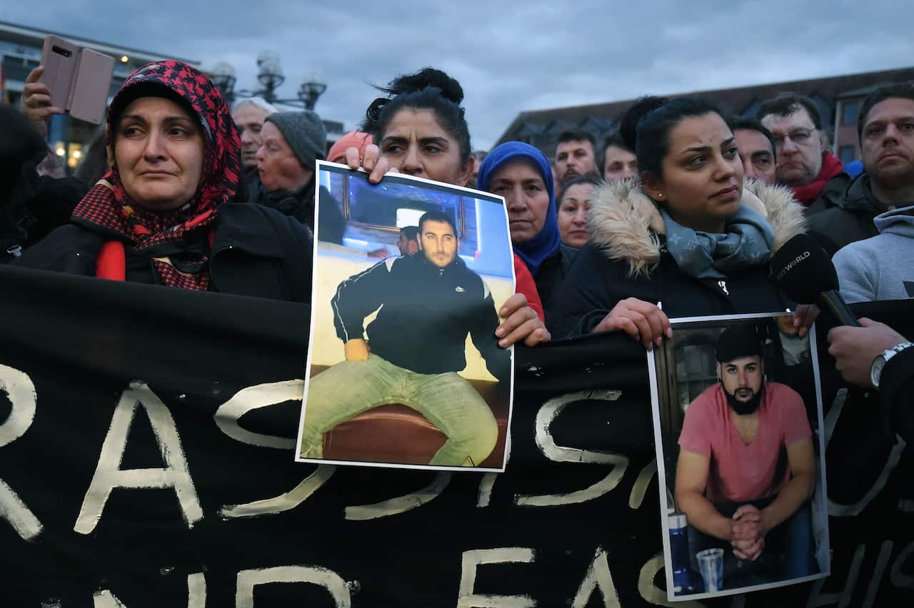 Mourners hold up photos, believed to be of victims, during a vigil close to a crime scene in Hanau, Germany